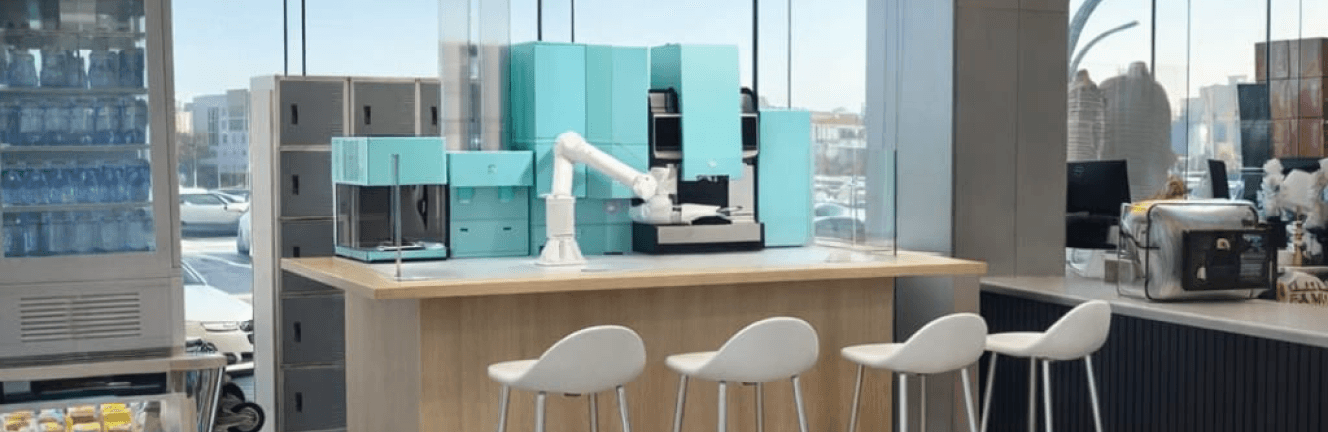 Modern automated robotic coffee bar with turquoise machines and a white robotic arm behind a light wood counter